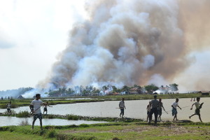 Ethnic Arakanese with weapons walking away from a village in flames while a soldier stands by. Arakan State, Burma, June 2012. © 2012 Private