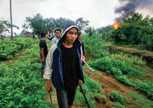 Ethnic Rakhine men lurk outside homes burned in one of the many episodes of violent conflict between Buddhist Rakhine and Muslim Rohingya communities, June 2012. Photo by Reuters.