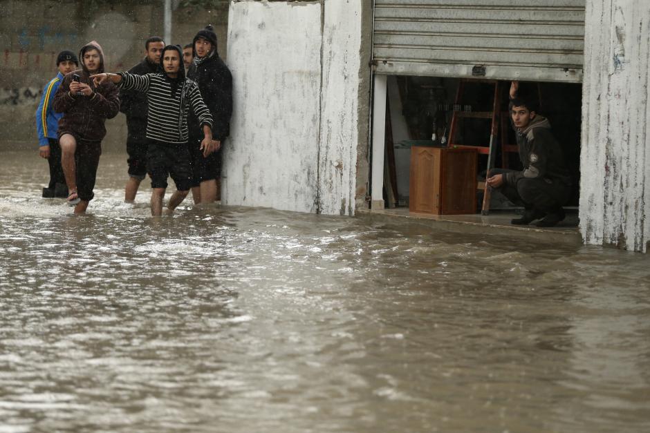A man looks out of his shop as Palestinians walk through a flooded road following heavy rain in Gaza City November 27, 2014. Mohammed Salem/Reuters