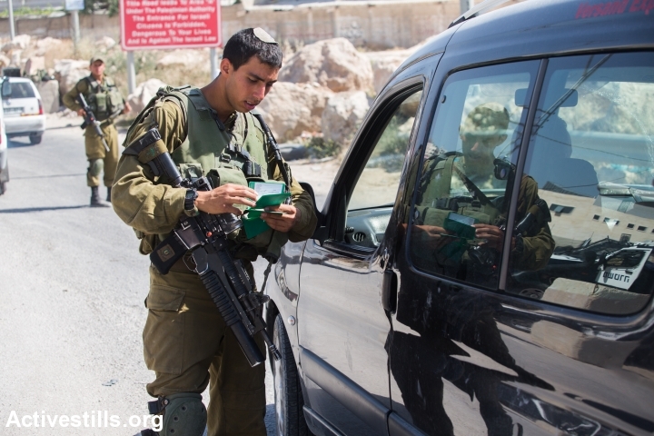 An Israeli soldier checks a Palestinian man’s documents at a checkpoint outside the West Bank city of Hebron on June 17, 2014, as the hunt for three Israeli teenagers believed kidnapped by militants entered its fifth day. Photo by Tess Scheflan/Activestills.org
