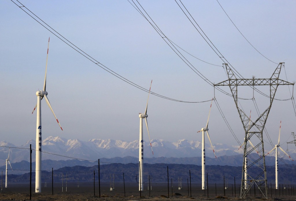 An electricity pylon is seen next to wind turbines at a wind power plant in Hami, Xinjiang Uighur Autonomous Region, China, March 21, 2015. China's wind farm firms are feeling the heat as state grid operators deliberately delay hooking them up and cut back on purchases, wasting about a fifth of the total wind power output or enough electricity to run Beijing for 40 days. Picture taken March 21, 2015. REUTERS/Stringer 