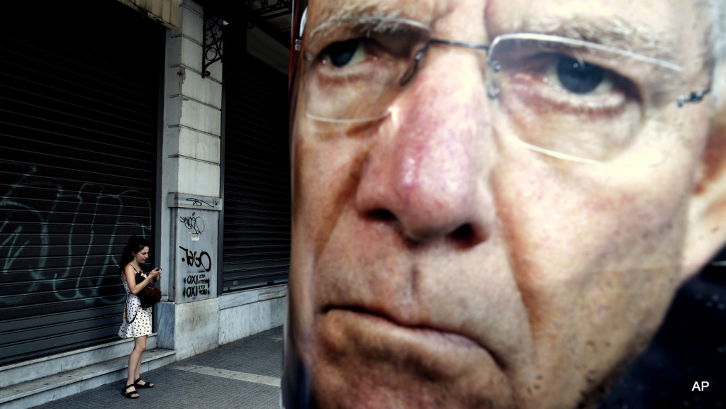 A woman uses her cell phone next to a poster depicting German Finance Minister Wolfgang Schaeuble placed by supporters of the No vote to the referendum in the northern Greek port city of Thessaloniki, Friday, July 3, 2015. Greeks will vote Sunday on whether to accept a proposal that creditors had made of specific reforms in exchange for loans. European Union institutions are framing it as a vote for or against the euro. (AP Photo/Giannis Papanikos)