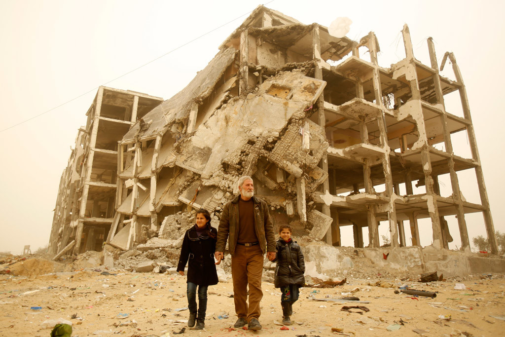 A man holds the hands of his granddaughters near the remnants of the residential towers where the girls used to live, in the city of Beit Lahia, in the northern Gaza Strip. Photo: UNICEF/Eyad El Baba