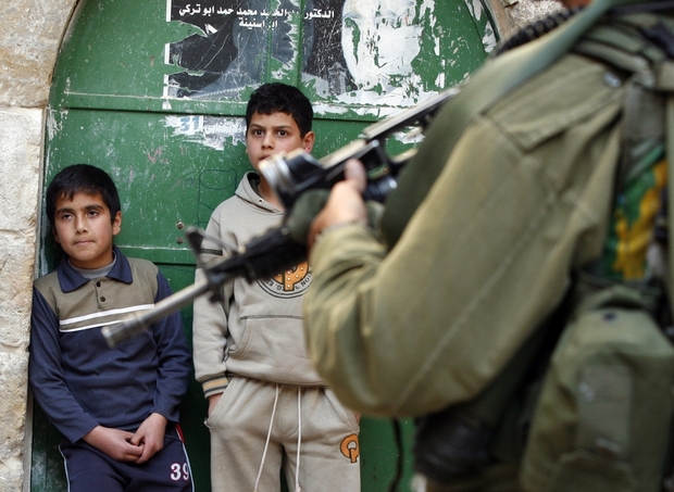 Photo: An Israeli soldier stands guard as Palestinian children look at a protest against Jewish settlements, near Beit Romano settlement in the city center of the occupied West Bank town of Hebron on 24 April, 2010 (AFP).