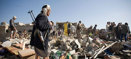 A Houthi Shiite fighter stands guard on Thursday [17 Dec] as people search for survivors under the rubble of houses destroyed by Saudi airstrikes near Sanaa Airport. (photo: AP)