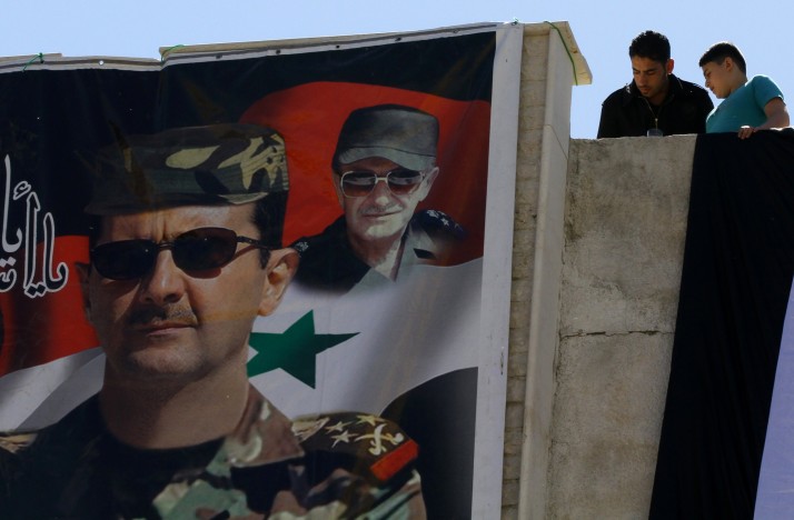 Syrians look down at a poster of Syrian President Bashar al-Assad | Louai Beshara/AFP/Getty Images
