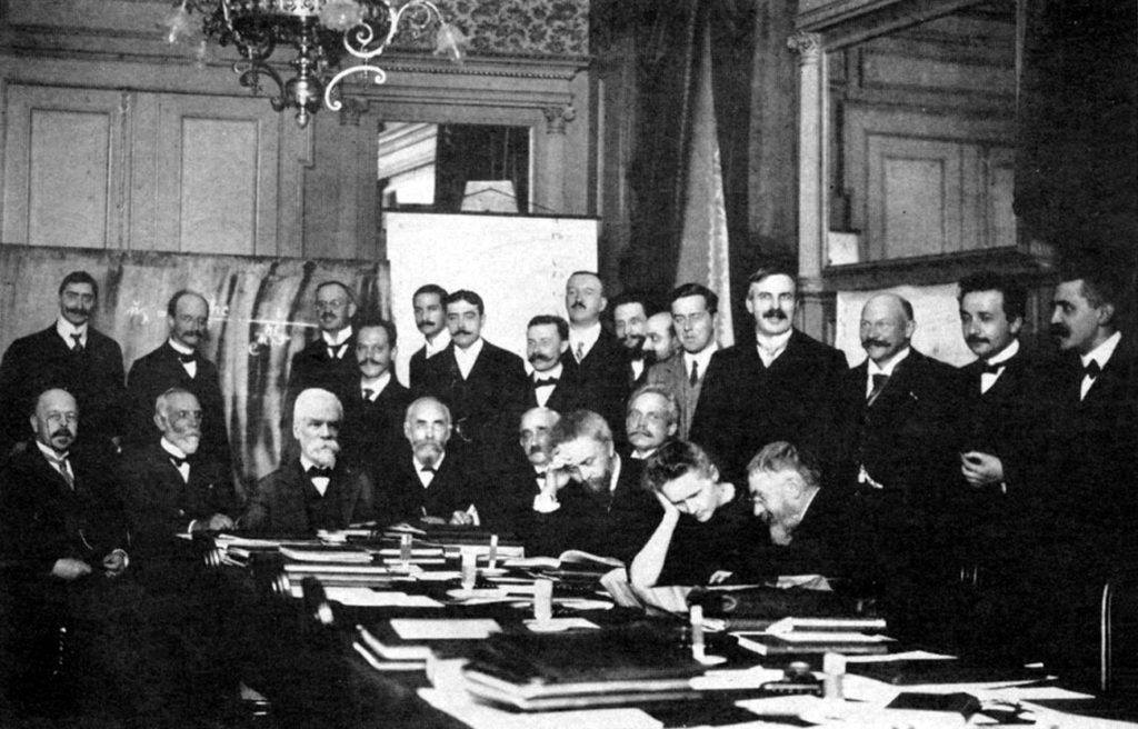 At the 1911 Solvay Conference. Curie leaning on table. Einstein second from right. Also in attendance: Max Planck, Henri Poincaré, and Ernest Rutherford.