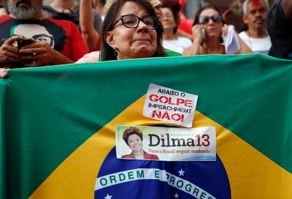 A demonstrator holds a Brazilian flag with a sticker that reads in Portuguese, “Down with the coup, impeachment no,” during a protest in support of President Rousseff and former President Lula da Silva in São Paulo, Brazil, March 31, 2016. Photo: Andre Penner/AP