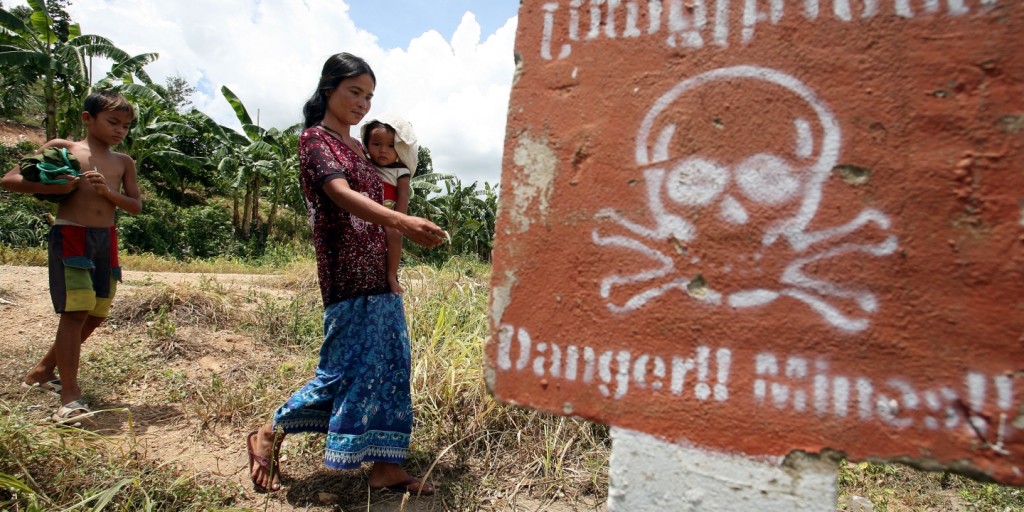 A woman carrying a baby walks by a land mine-awareness sign in the village of O’Chhoeu Kram in Cambodia. Photo: Tang Chhin Sothy/AFP/Getty Images