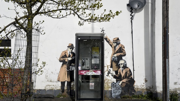 New Banksy artwork. The new graffiti street art piece, suspected of being a Banksy, which appeared on the side of a house on Fairview Road adjacent to St. Anne's Terrace, Cheltenham. The artwork, which shows three figures listening into a conversation at a telephone box, is just a few miles away from Government Communications Headquaters (GCHQ), which is responsible for providing signals intelligence and information assurance to the British Government and Armed Forces. Picture date: Monday April 14, 2014. The Gloucestershire Echo reported that the owner of the house, Karren Smith, 48, said she saw men packing a white tarpaulin into a van at about 7.30am on Sunday. Photo credit should read: Ben Birchall/PA Wire URN:19564819