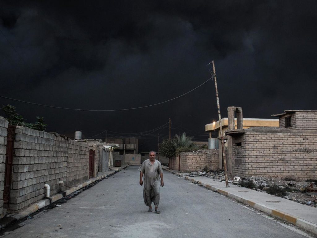 An Iraqi man walks on a street covered with smoke after an oil fire was set ablaze in the Qayyarah area, south of Mosul AFP/Getty