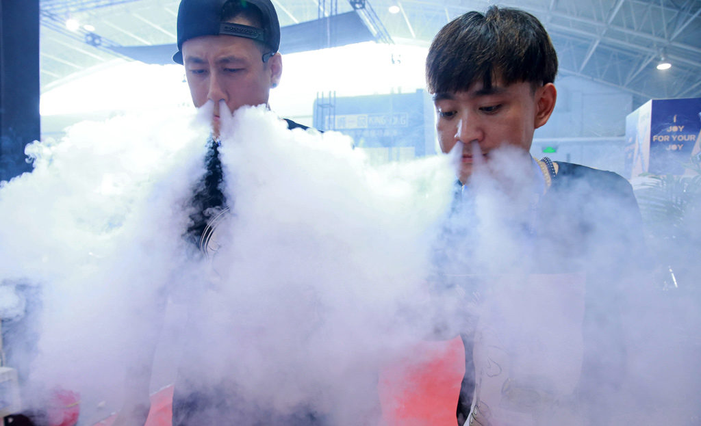 Sales staff exhale vapor while demonstrating their electronic cigarette products at the Vape China Expo at the China International Exhibition Center in Beijing on July 23, 2015. Photo: STR/AFP/Getty Images