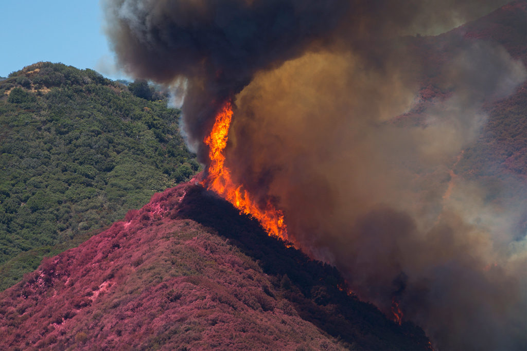 Flames threaten to jump a ridge that firefighting aircraft have painted red with fire retardant above Cajon Boulevard at the Blue Cut Fire on Aug. 18, 2016, near Wrightwood, California. Photo: David McNew/Getty Images