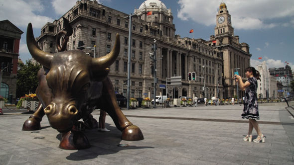 China today: a tourist snaps the bull of capitalism in front of Shanghai’s Bund hotel, bedecked with communist flags. Bruno Sorrentino and John Pilger